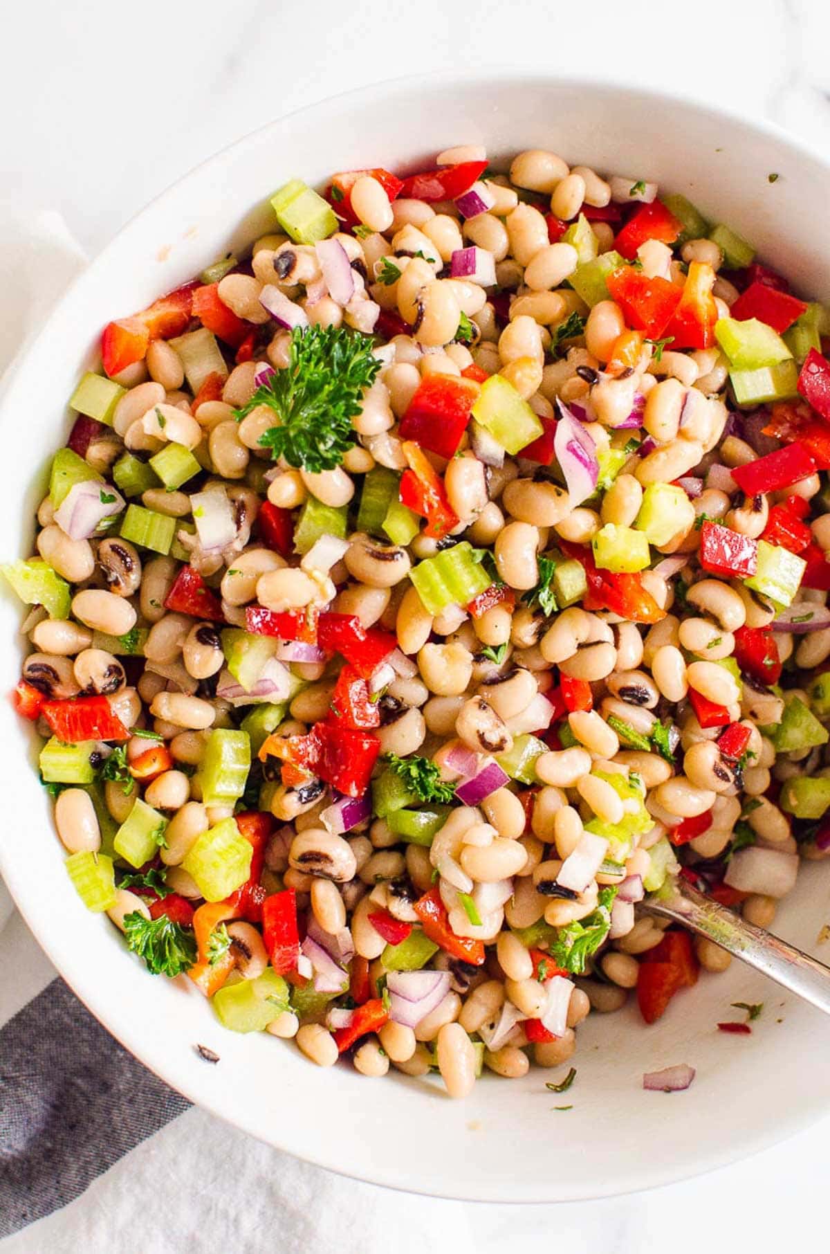 White bean salad in a white bowl with serving spoon.