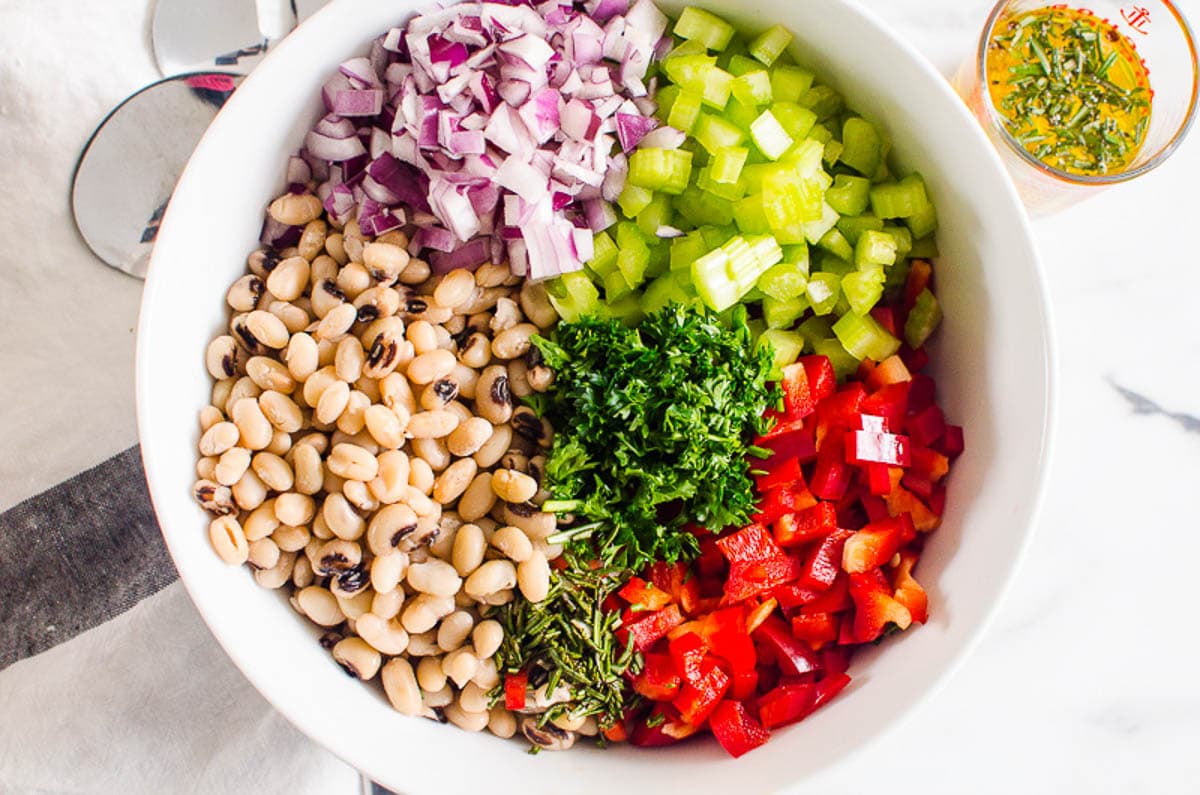 White beans, red onion, celery, red bell pepper, parsley in white bowl. Vinaigrette in a jar.