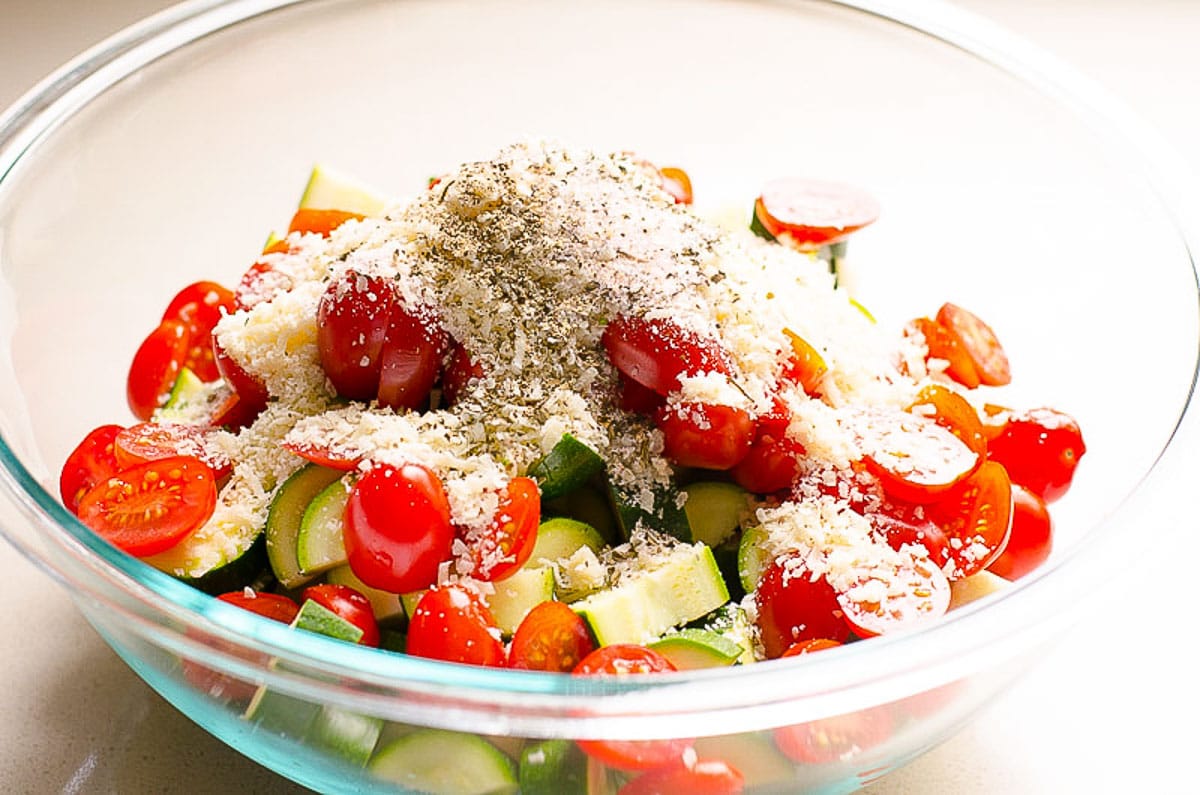 Chopped zucchini and tomatoes with herbs and parmesan cheese in a bowl.