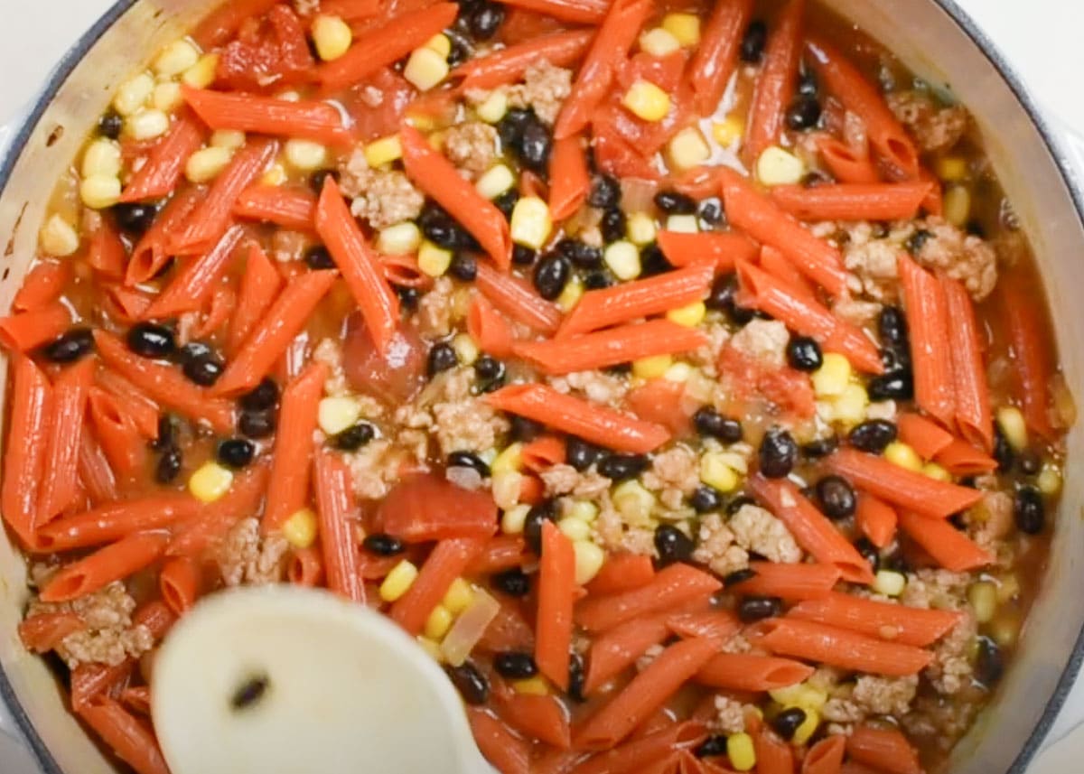 Pasta, beans, corn, meat and broth in a pot.