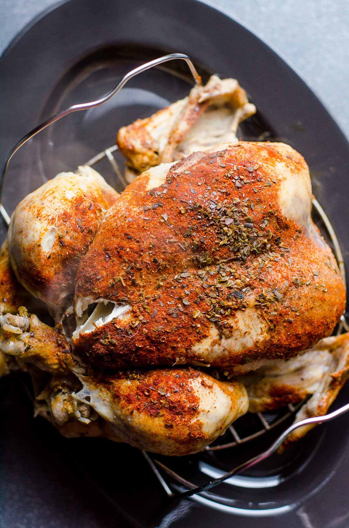 Whole roasted chicken on trivet on gray platter.