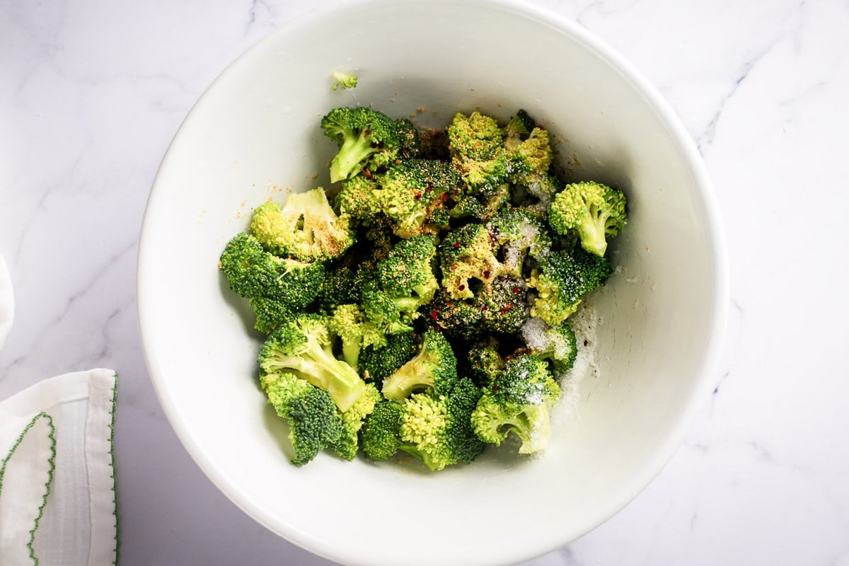 Fresh broccoli with seasonings in white bowl.