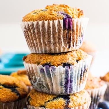 Three healthy almond flour blueberry muffins stacked on top of each other.