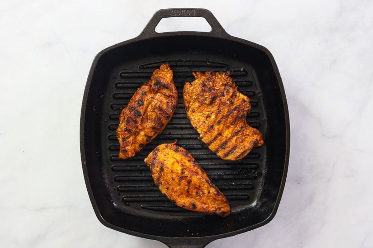 Marinated chicken breasts cooked on a cast iron skillet.