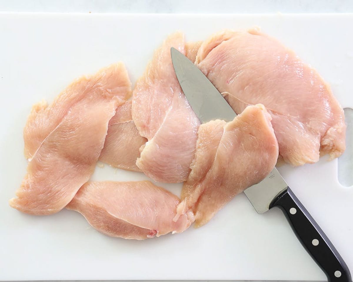 Cutting chicken breasts with a knife on cutting board.