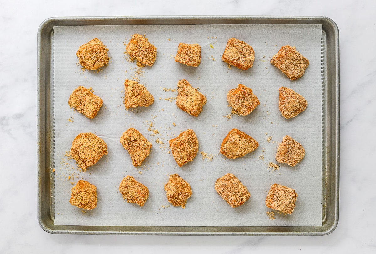 Unbaked chicken nuggets on baking sheet lined with parchment paper.