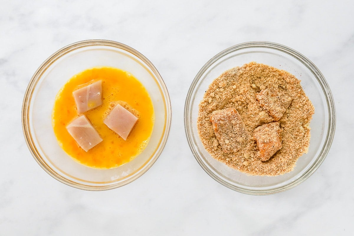 Cubed raw chicken in a bowl with eggs, cubed chicken coated in almond flour mixture.