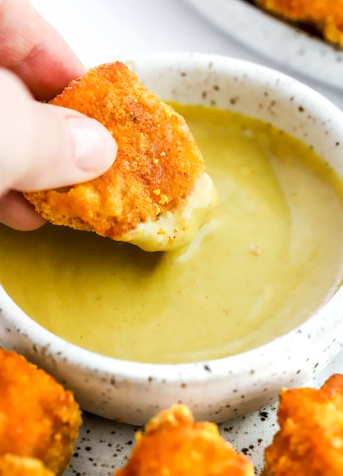 Hand dipping a chicken nugget into a bowl with honey mustard sauce.