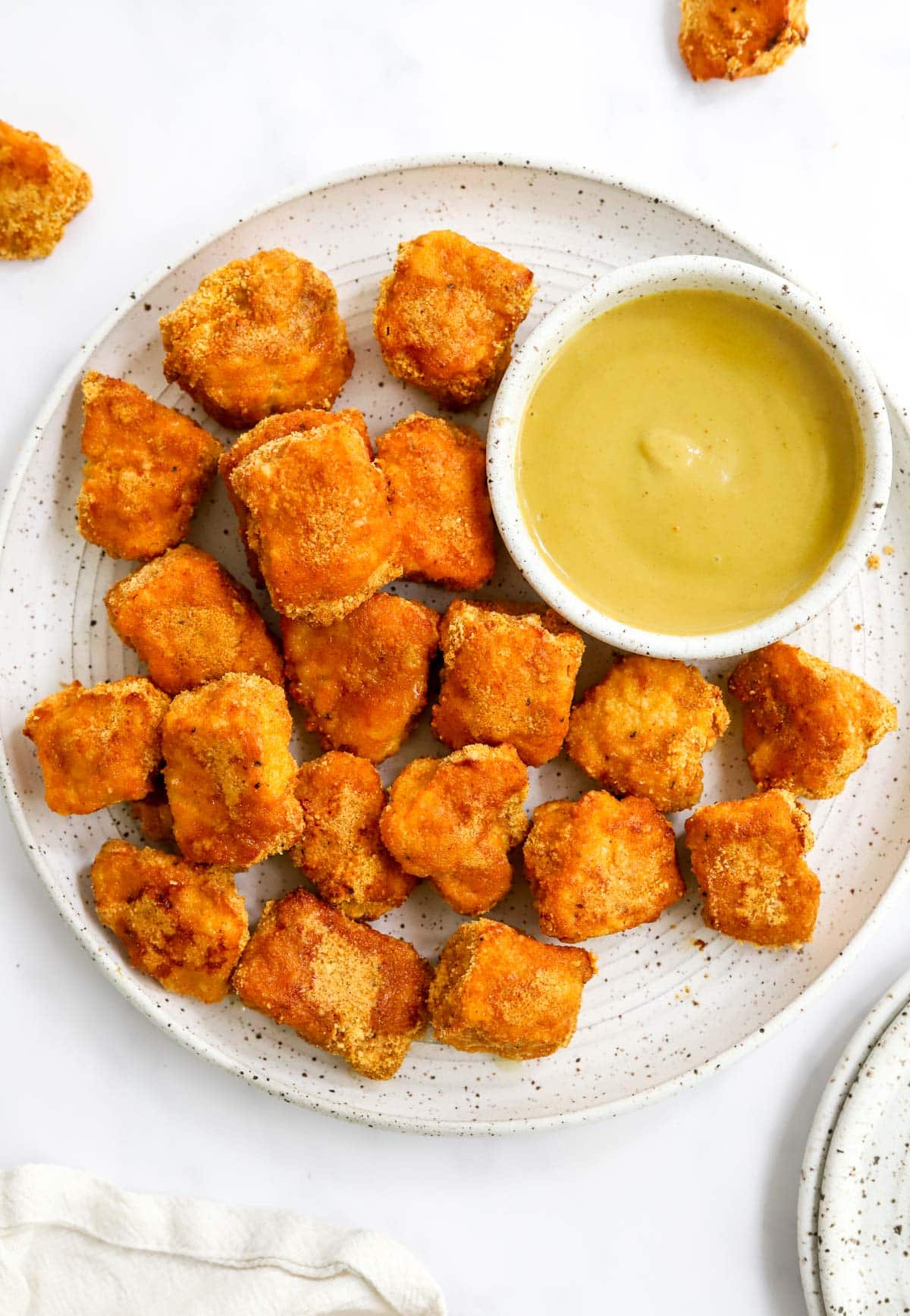 Chicken nuggets on a white plate with a small bowl of honey mustard dressing on the side.