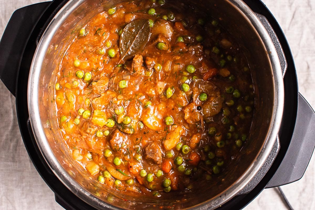 Thickened beef stew with peas and carrots in pressure cooker pot.