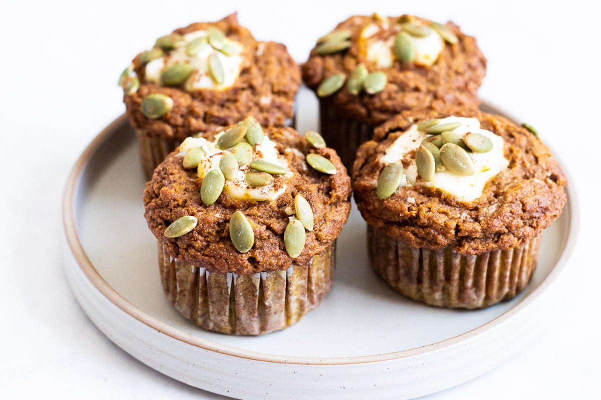 Four healthy pumpkin muffins with cream cheese and pepitas on a plate.