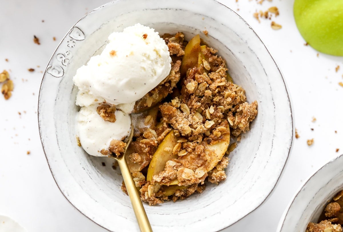 Healthy apple crisp in a bowl with spoon and vanilla ice cream.