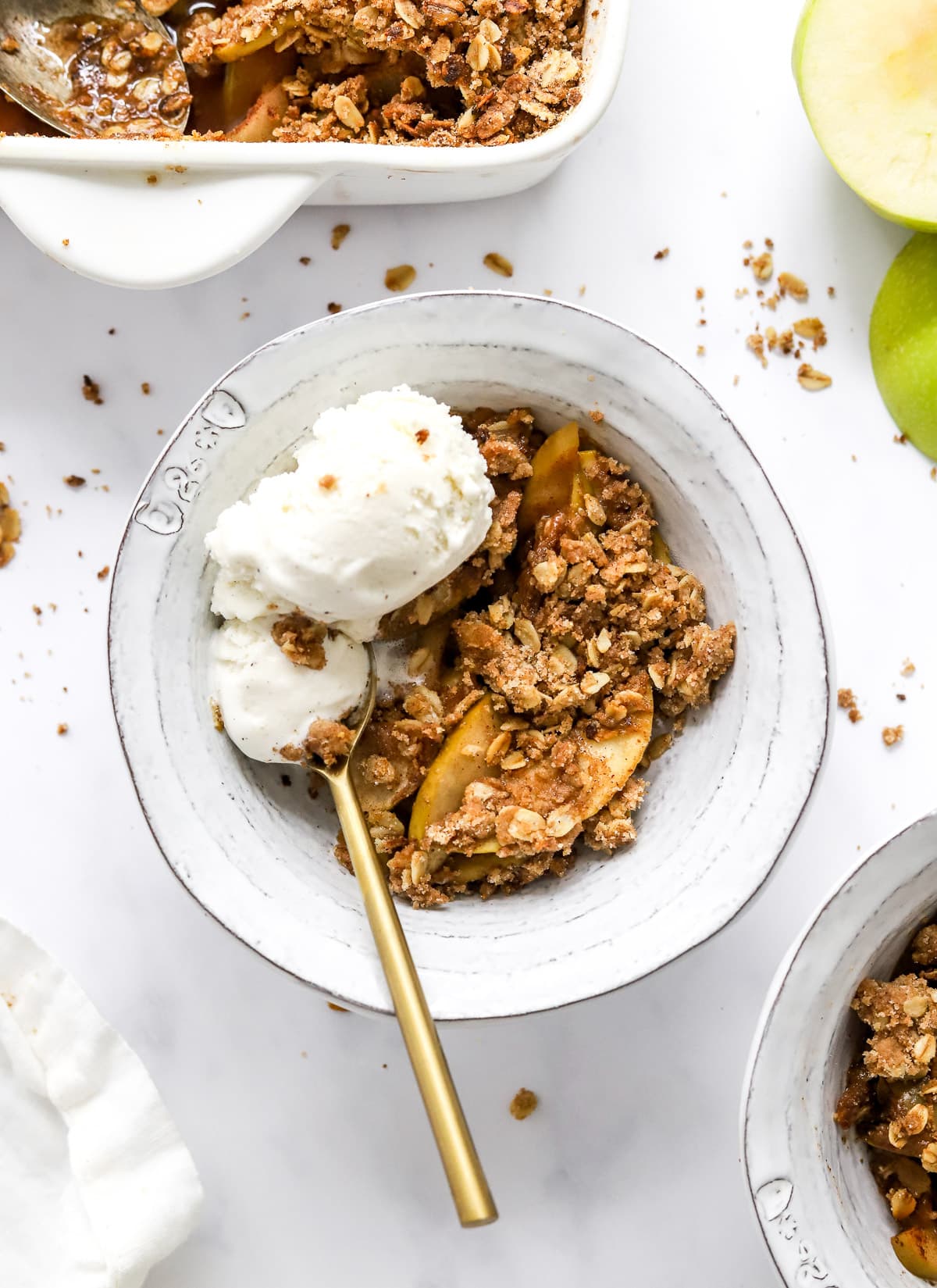 Healthy apple crisp in a bowl with ice cream and baking dish with crisp. 