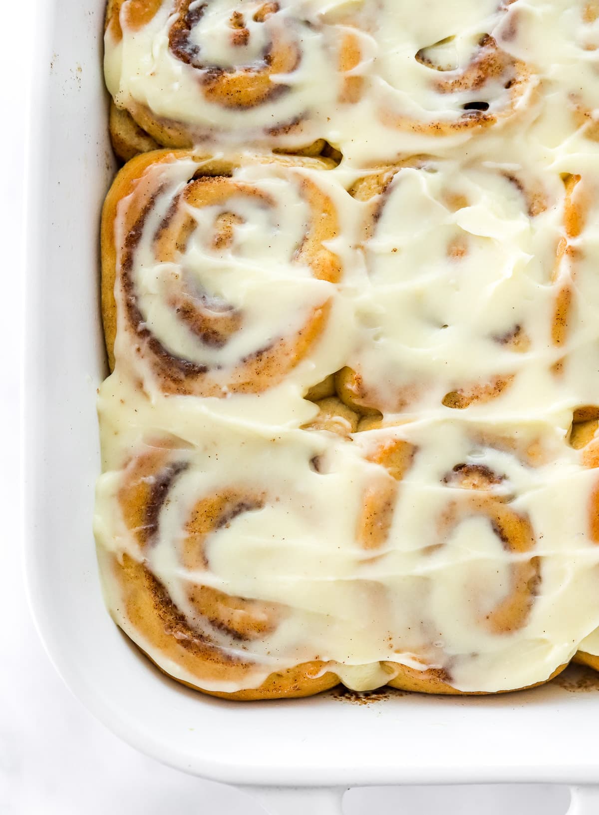 Healthy cinnamon rolls spread with frosting in baking pan.