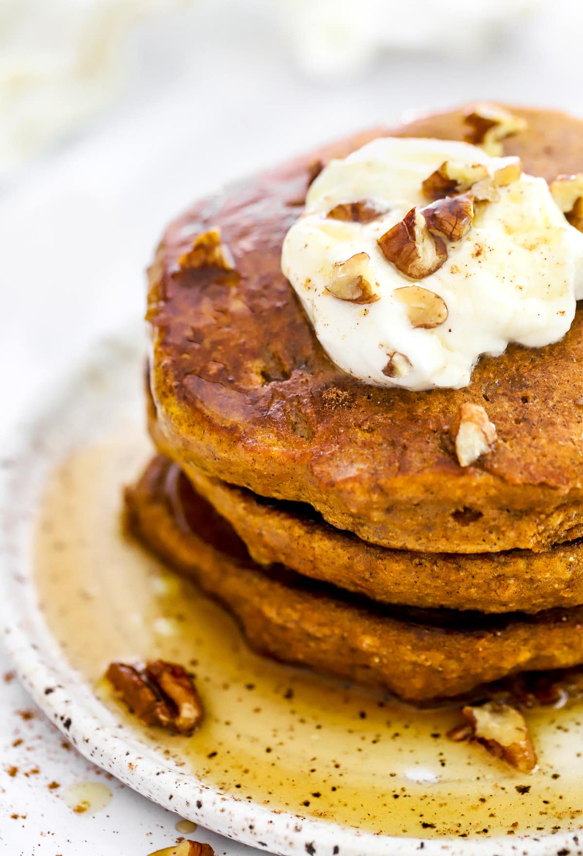 Close up of a stack of three healthy pumpkin pancakes with pecans, maple syrup and yogurt.