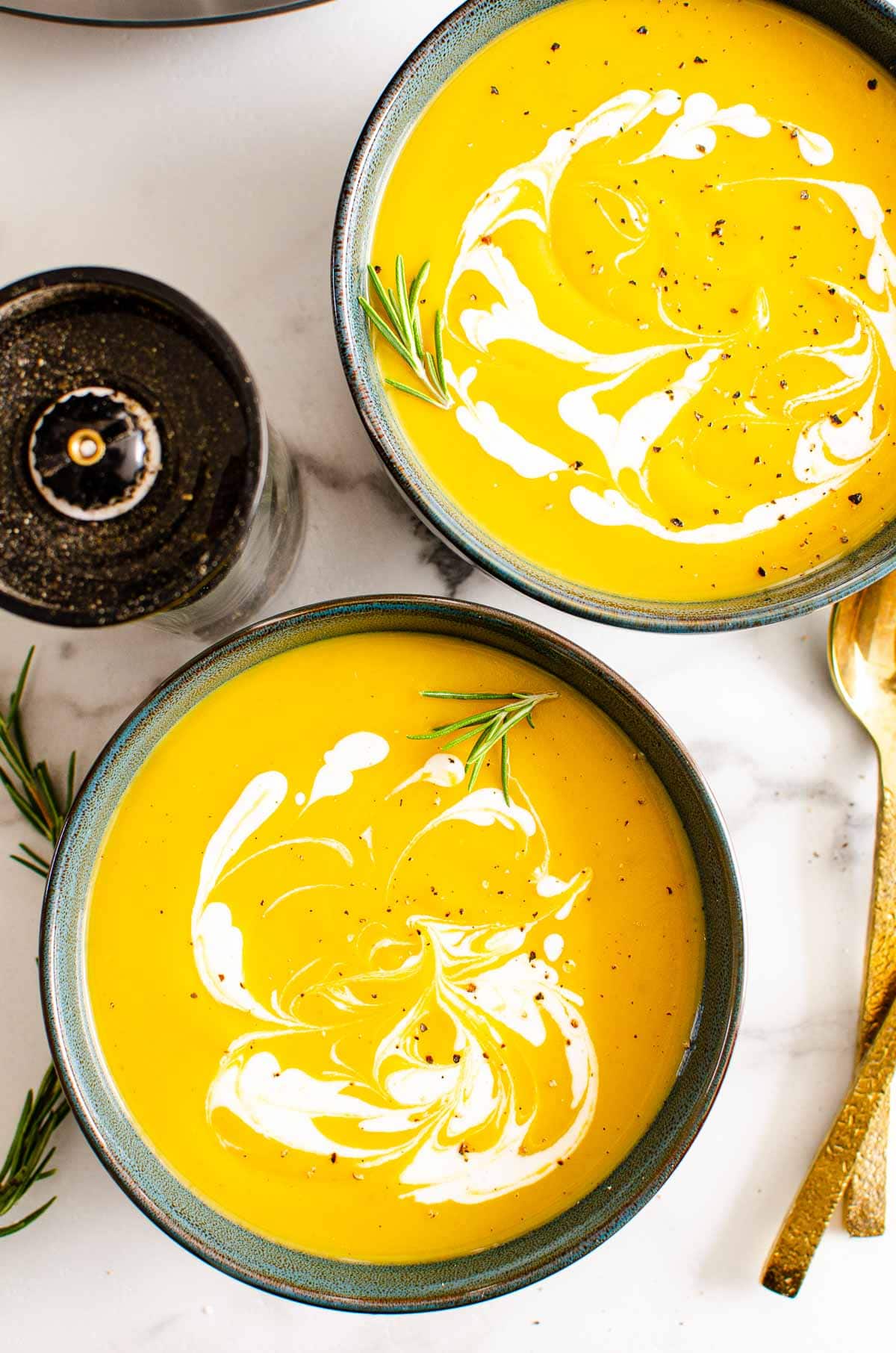 Two bowls with Instant Pot butternut squash soup garnished with cream and black pepper.