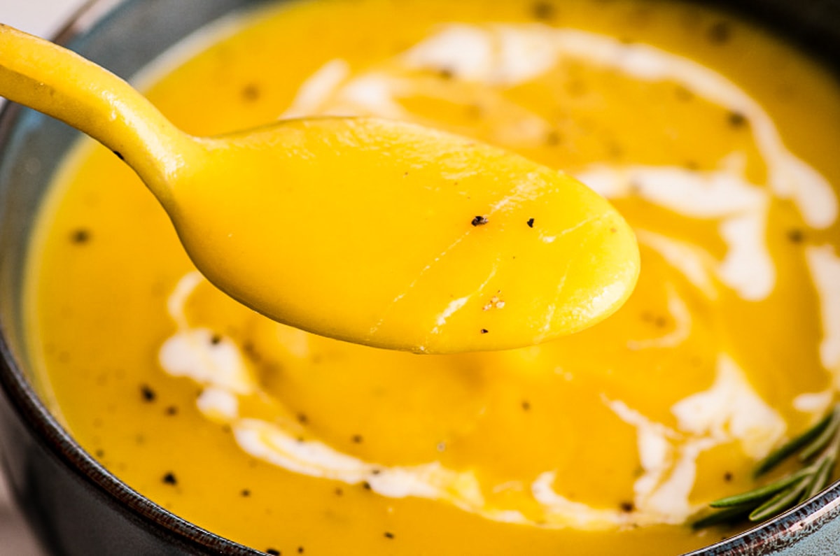 Butternut squash soup with cream and pepper on a spoon.