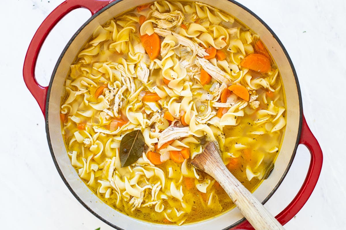 Turkey noodle soup in red pot with wooden spoon.