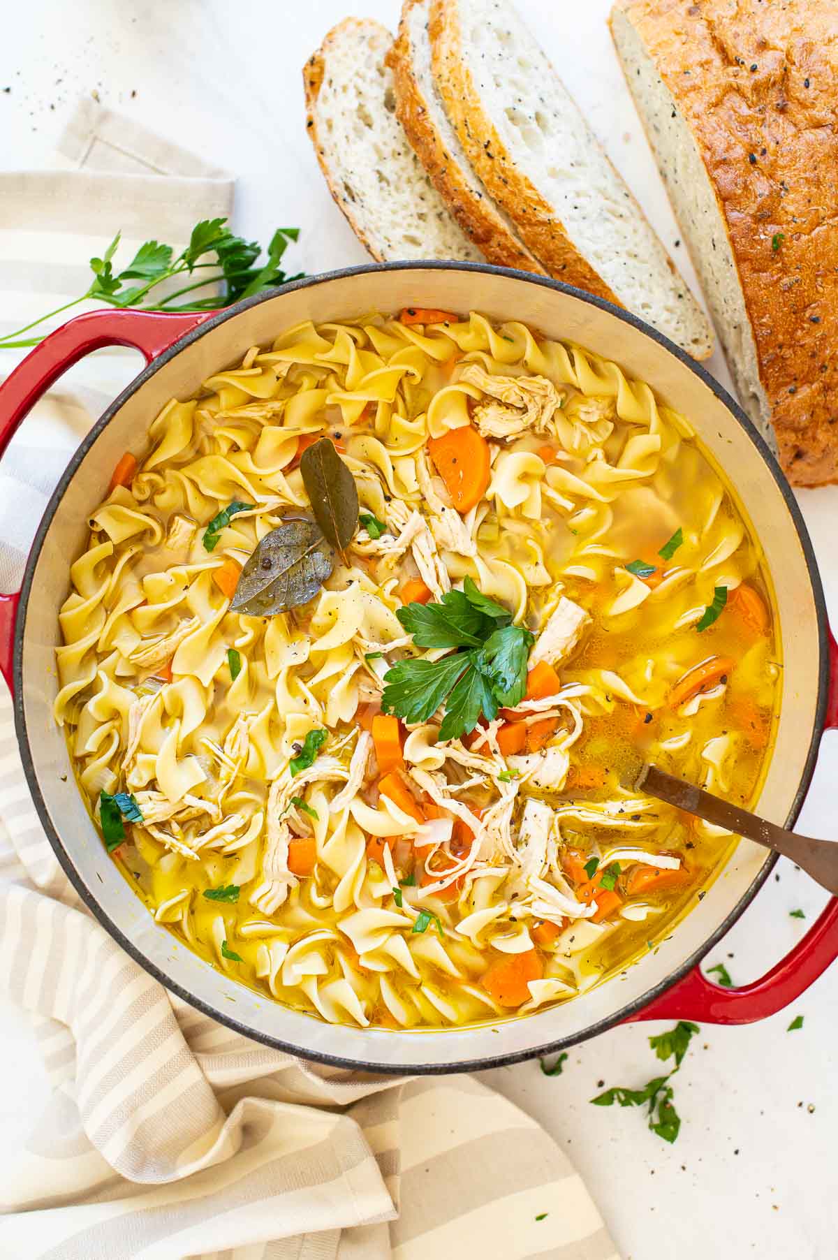 Turkey noodle soup in pot with ladle and pepper jar in background.