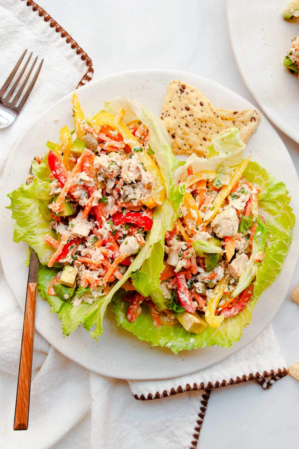 Canned salmon salad in lettuce cups on a plate with a fork, chips and napkin underneath.