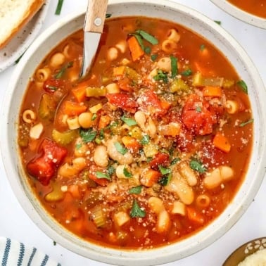 Vegetarian pasta fagioli in a bowl with a spoon with bread and parmesan cheese.