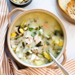 Creamy green borscht in a bowl with spoon and bread and linen on a counter.