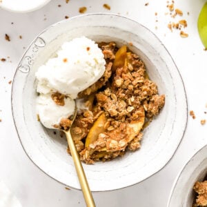 Healthy apple crisp in a bowl with ice cream and spoon.