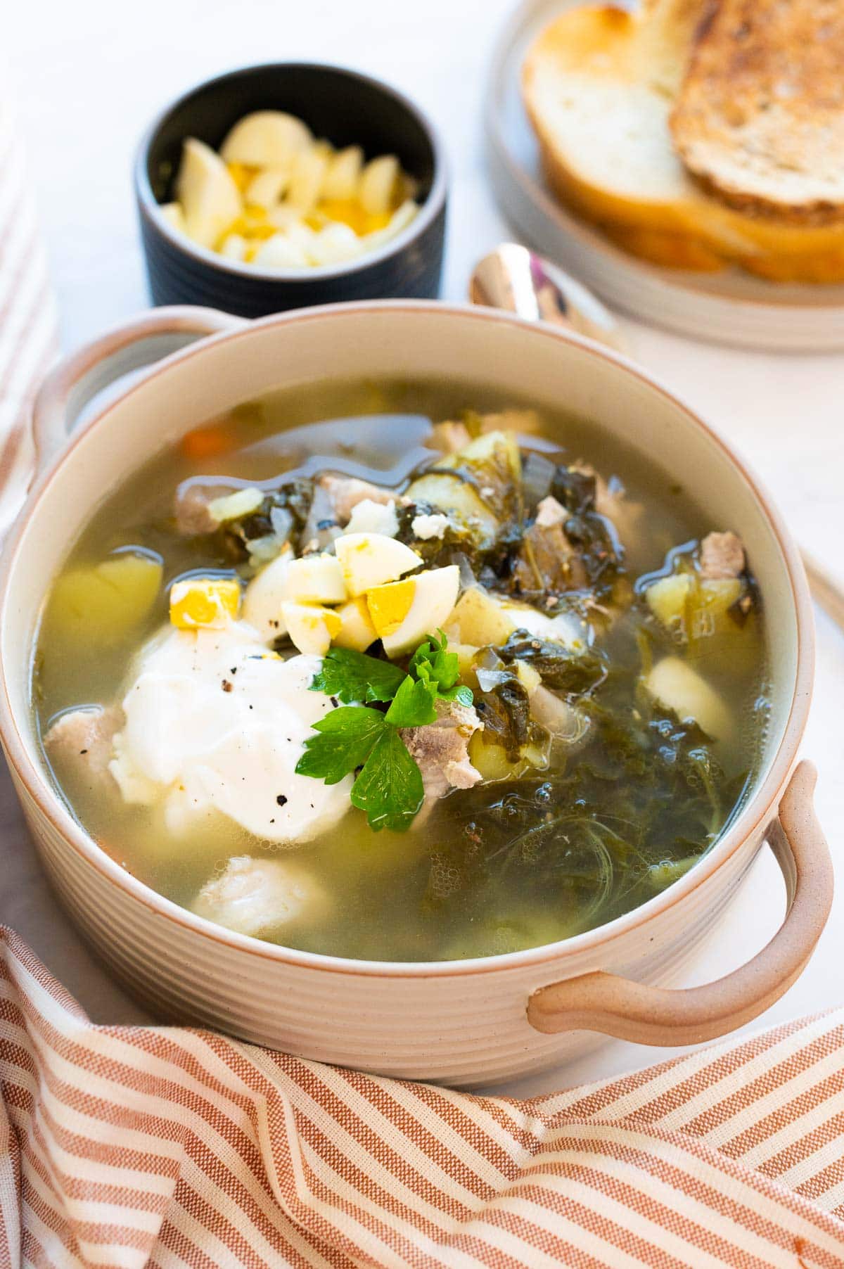 Green borscht served with a dollop of sour cream and hard boiled eggs in a bowl.