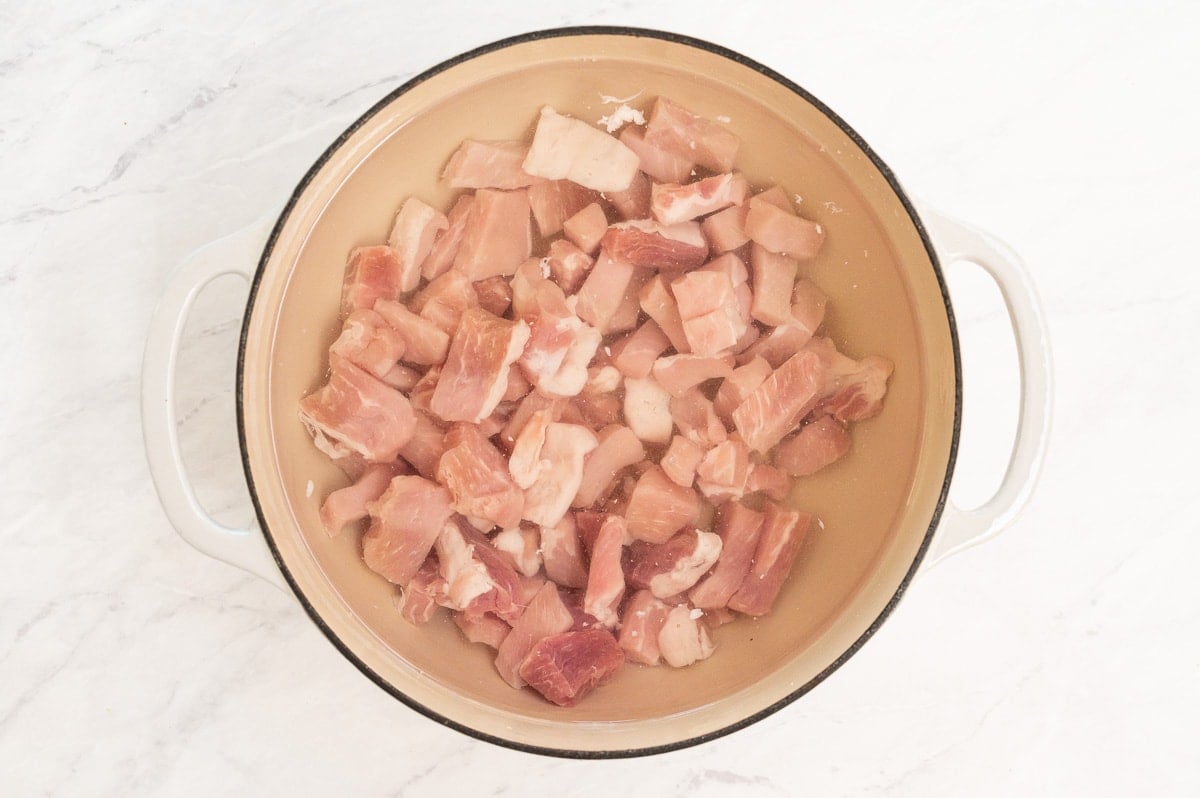 Cubed pork chops with cold water in white pot.