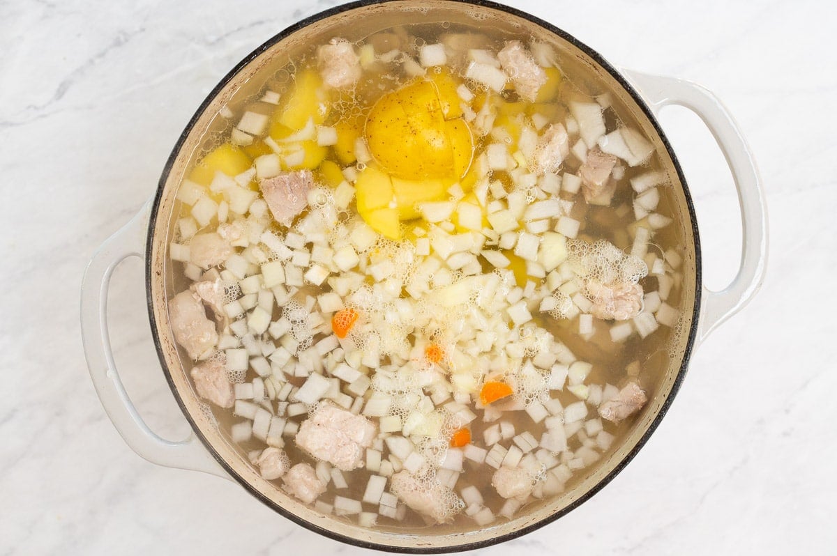 Diced onion, potatoes and carrots in pork broth in a pot.