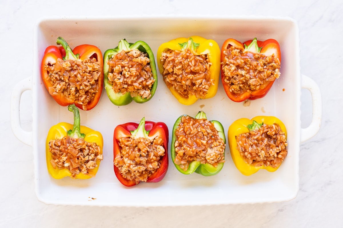 Eight unbaked pepper halves with stuffing in baking dish.