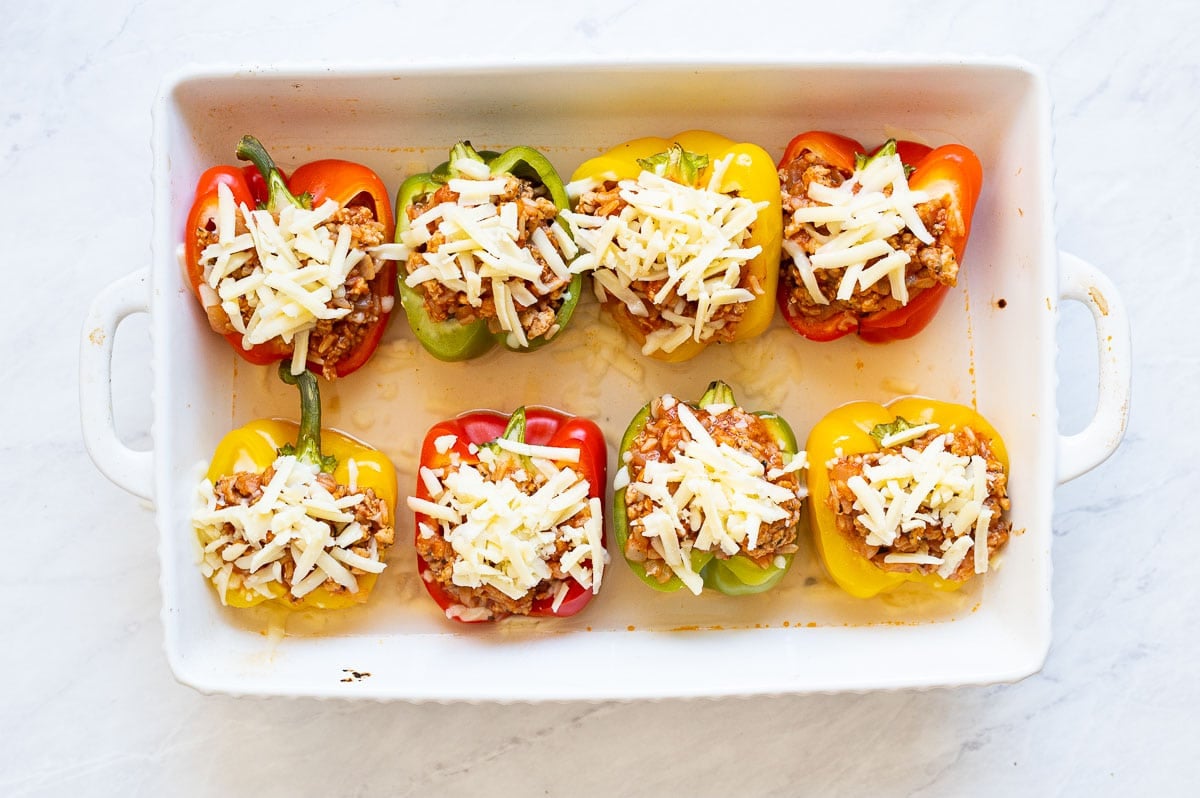 Eight stuffed bell peppers with cheese in a baking dish.