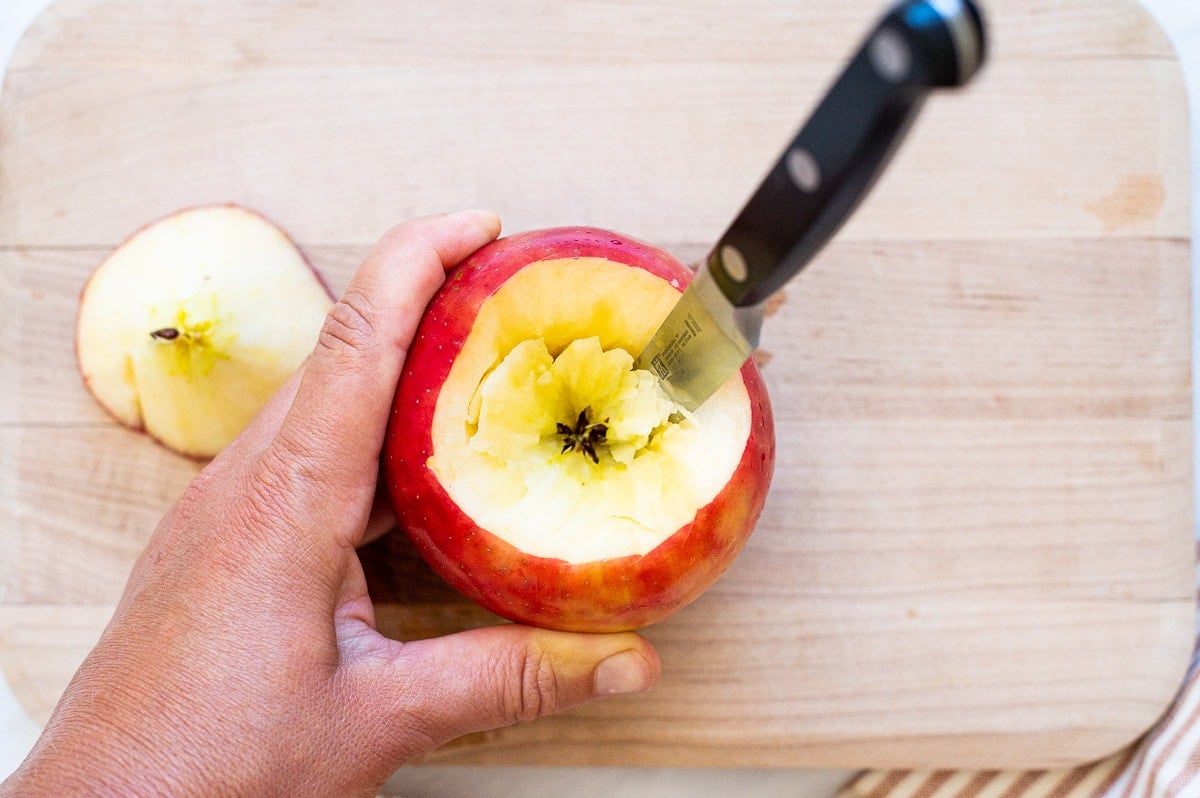 An apple on a cutting board with a knife in the core and the core removed.
