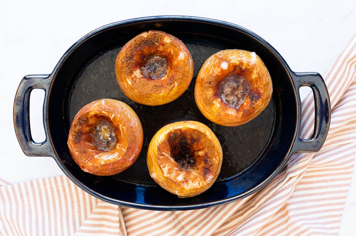 Four baked apples in a baking dish.