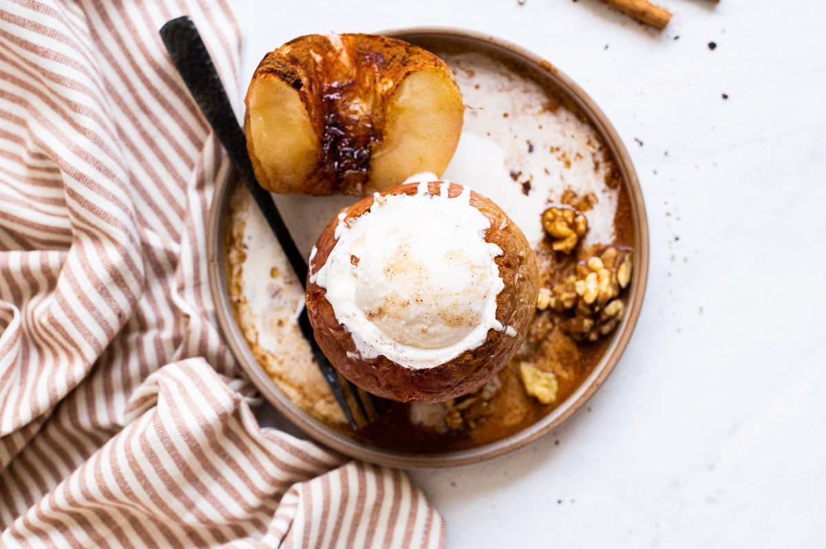 Healthy baked apples on a plate with one apple cut in half and the other topped with ice cream. 