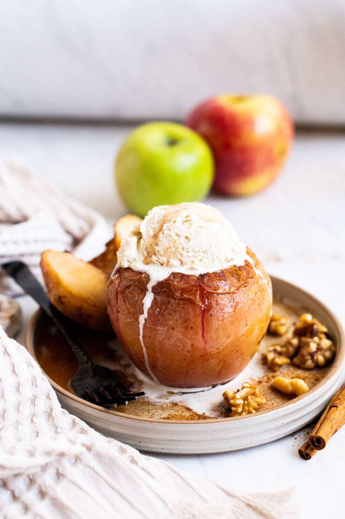 Healthy baked apple with a scoop of vanilla ice cream on a plate with a fork. Fresh apples in background.