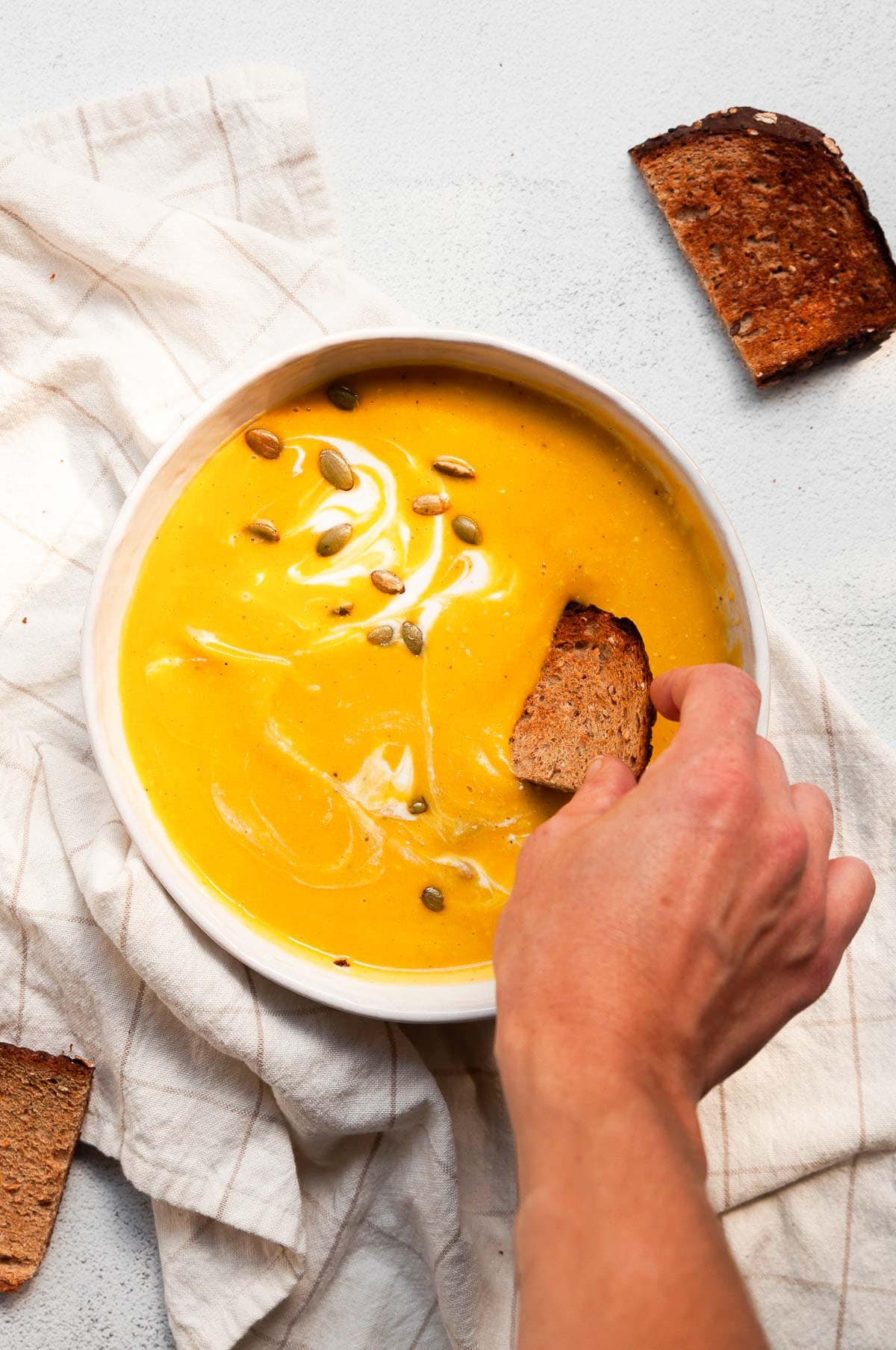 Hand dipping toast into a bowl with butternut squash soup.