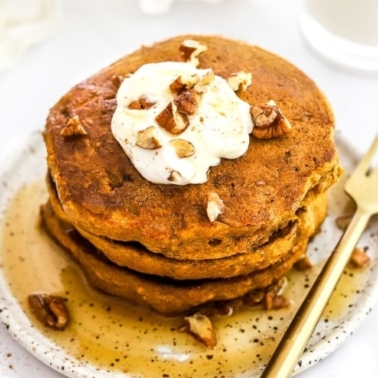 A stack of healthy pumpkin pancakes with a dollop of whipped topping and syrup.