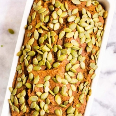 Healthy pumpkin bread in a loaf pan garnished with pumpkin seeds.