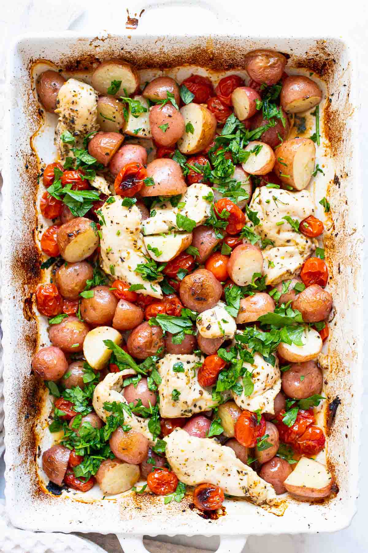 One pan chicken and potatoes with grape tomatoes and parsley in baking dish.