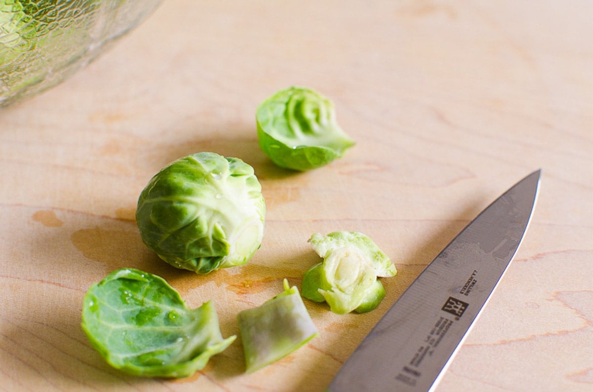 Trimmed brussels sprouts on cutting board with a knife.