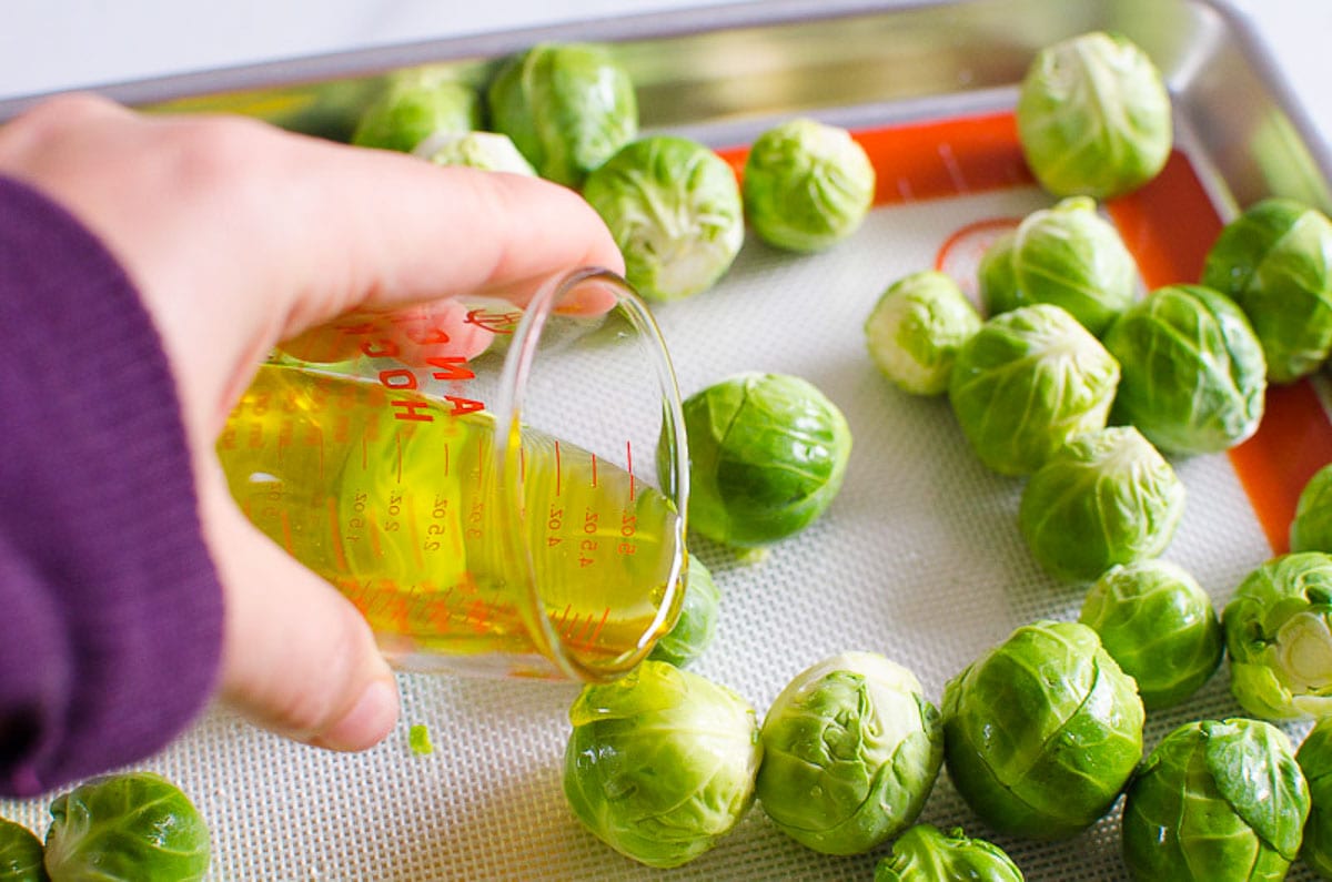 Drizzling brussels sprouts on baking sheet with olive oil.