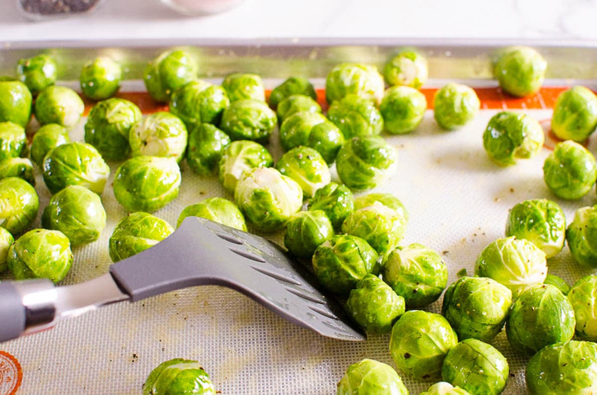 Brussels sprouts on a baking sheet with spatula.