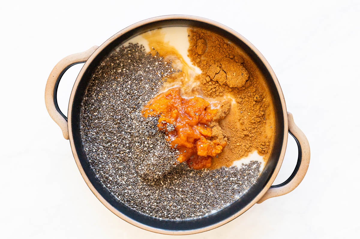 Milk, pumpkin puree, chia seeds, vanilla extract, maple syrup and pumpkin pie spice in black bowl.