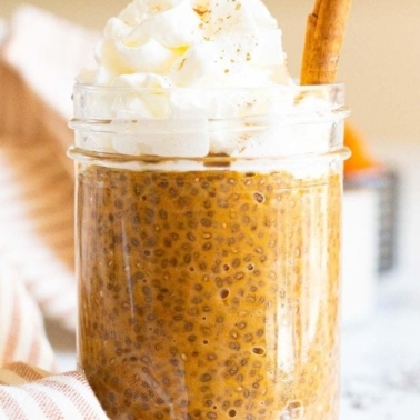 Pumpkin chia pudding in a jar with whipping topping and cinnamon stick.