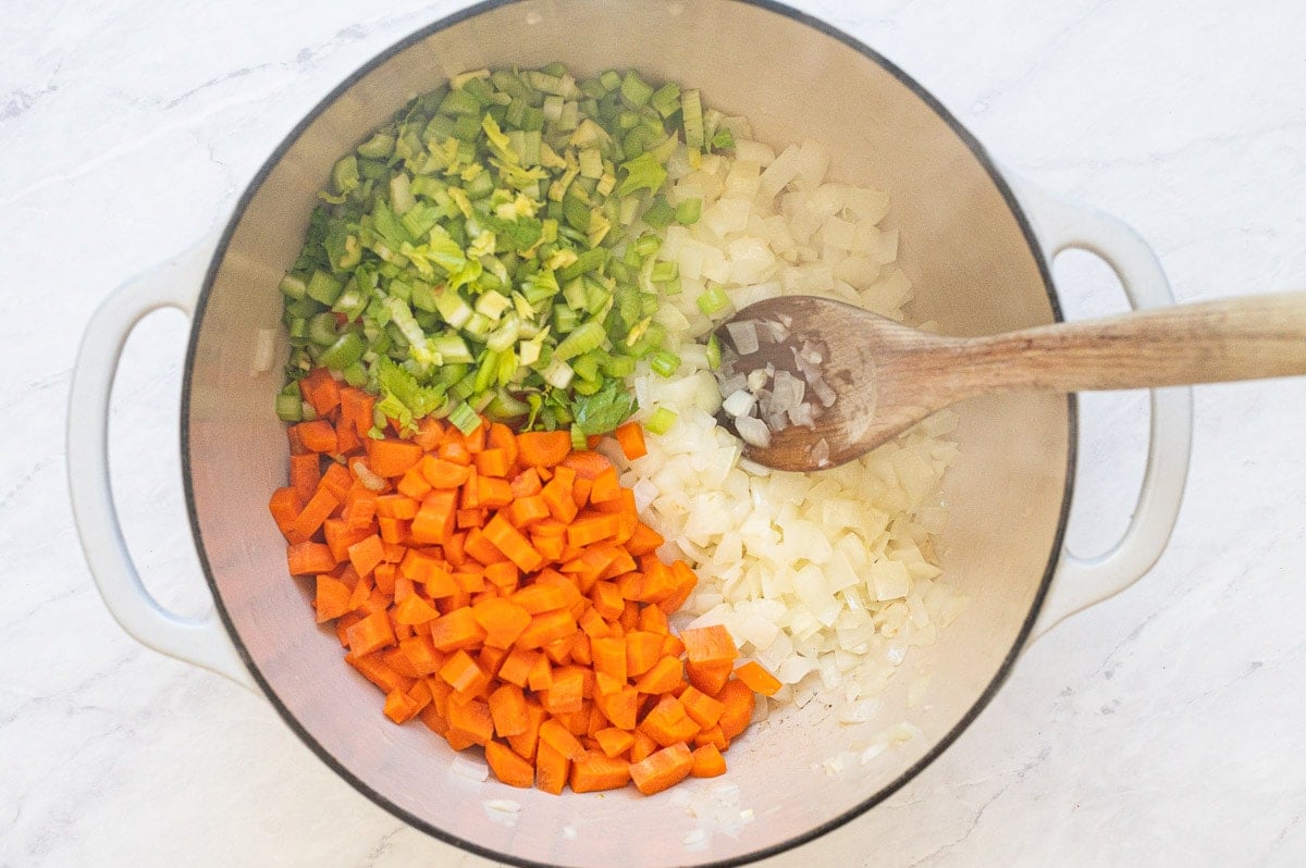 Diced onion, carrots and celery in white pot with wooden spoon.