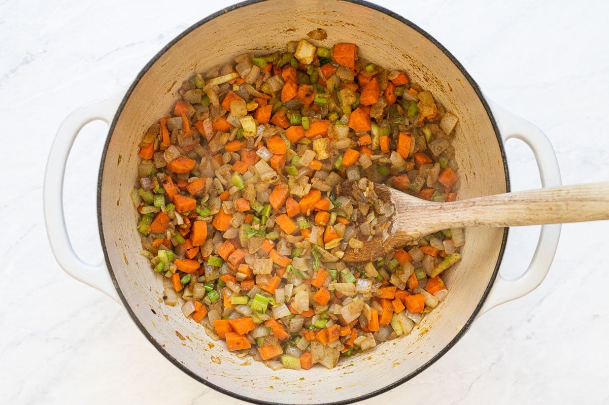 Sauteed veggies with spices in a pot with wooden spoon.