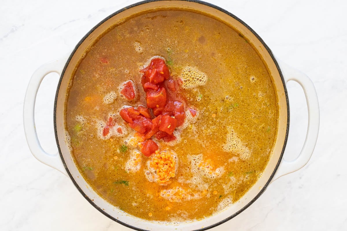 Broth, red lentils and diced tomatoes in white pot.