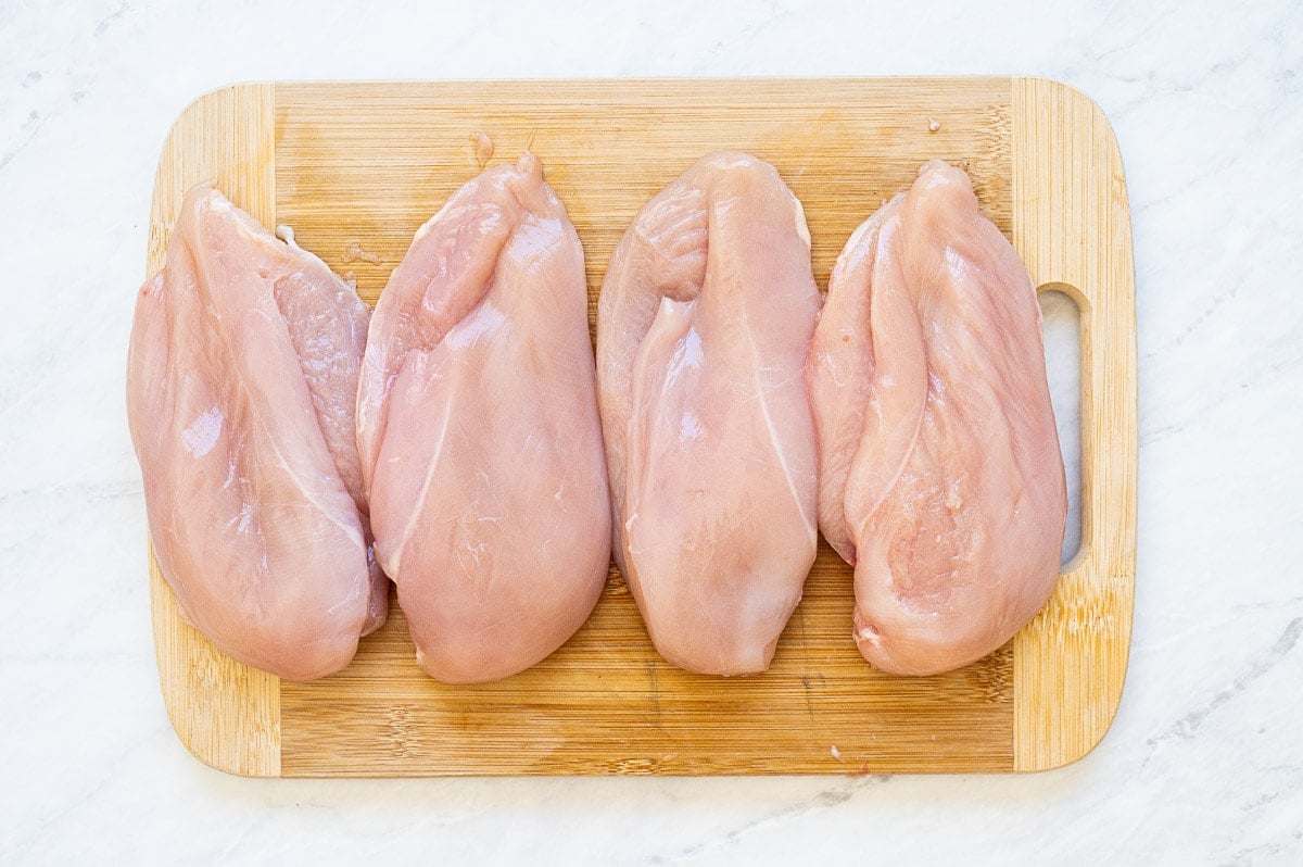 Four chicken breasts cut open to create a pocket on a cutting board.