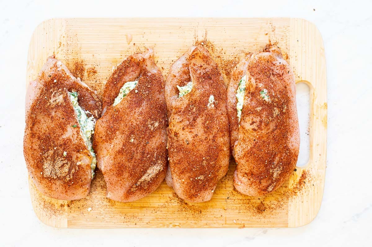 Four stuffed and seasoned chicken breasts on a wooden board.
